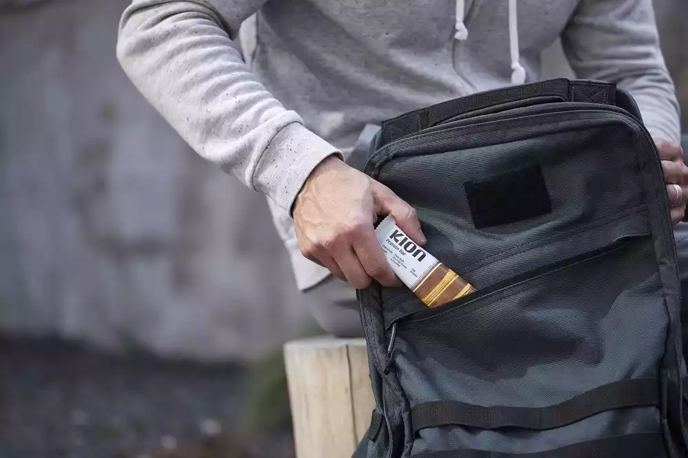 Man putting Kion Chocolate Crunch Protein Bar into his backpack