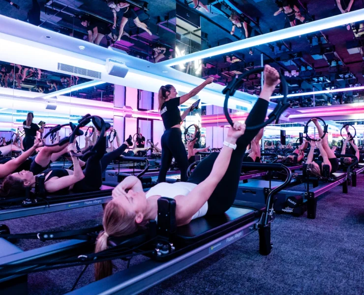 woman works out on a Reformer inside a Vaura Pilates studio, owned by F45