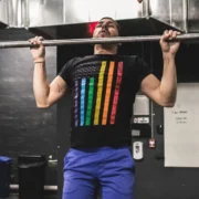 Man wearing pride t-shirt and doing a pull up at a gym.