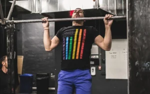 Man wearing pride t-shirt and doing a pull up at a gym.