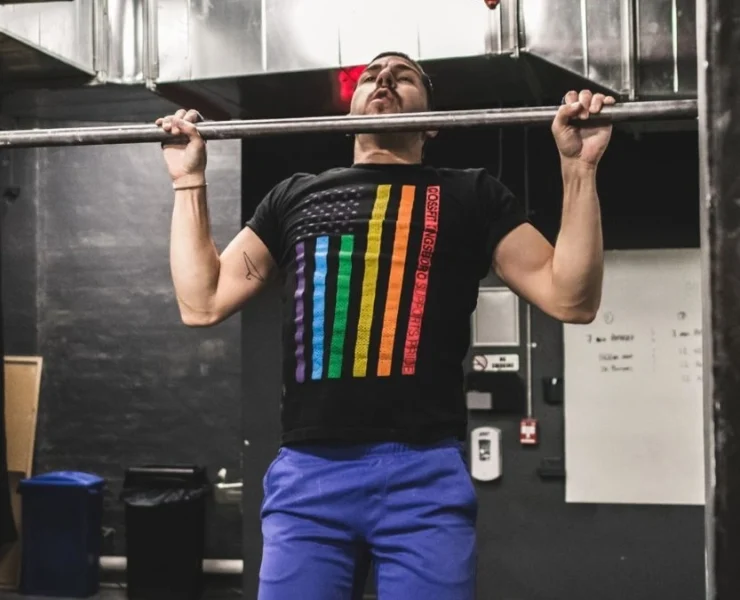 Man wearing pride t-shirt and doing a pull up at a gym.