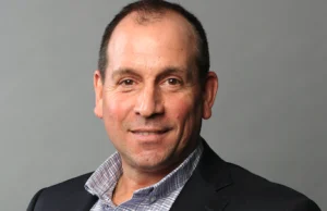 A smiling headshot of Andrew Alfano against a grey background.