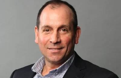 A smiling headshot of Andrew Alfano against a grey background.