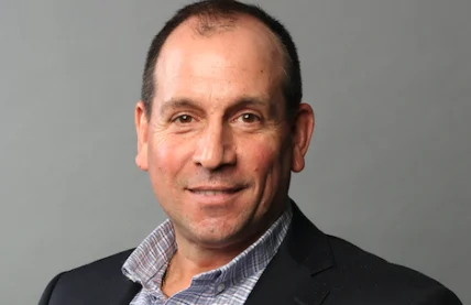 A smiling headshot of Andrew Alfano against a grey background.