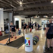 Group of people in a gym setting learning about lifting weights with an Olympic bar