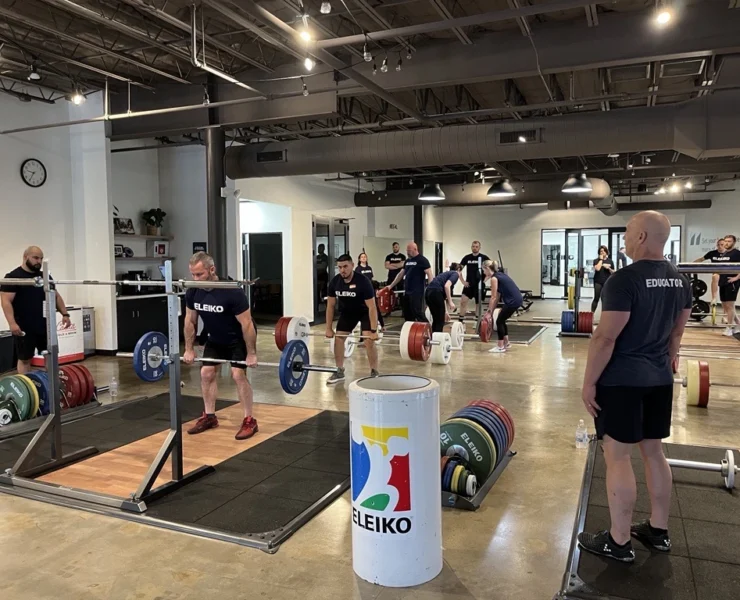 Group of people in a gym setting learning about lifting weights with an Olympic bar