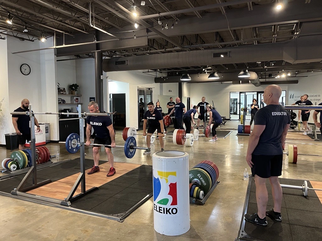 Group of people in a gym setting learning about lifting weights with an Olympic bar