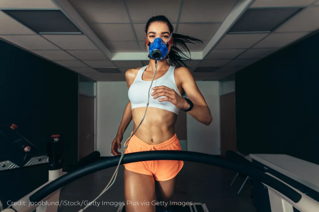 An image of woman running on a treadmill as her VO2 max is tested. The female is wearing a mask that determines Vo2 levels. 