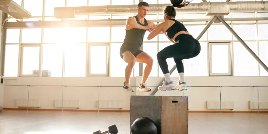 man and woman in gym doing box jump