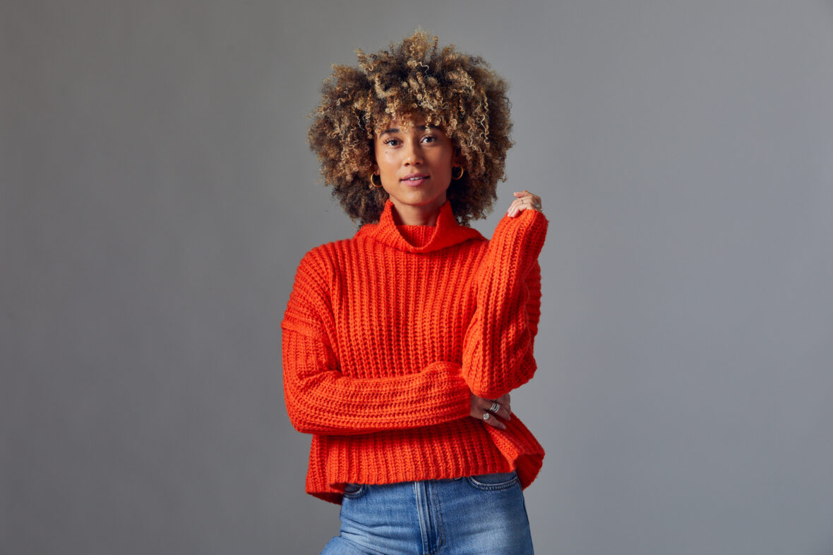 A headshot of Peloton instructor Ally Love in a red sweater against a gray background.