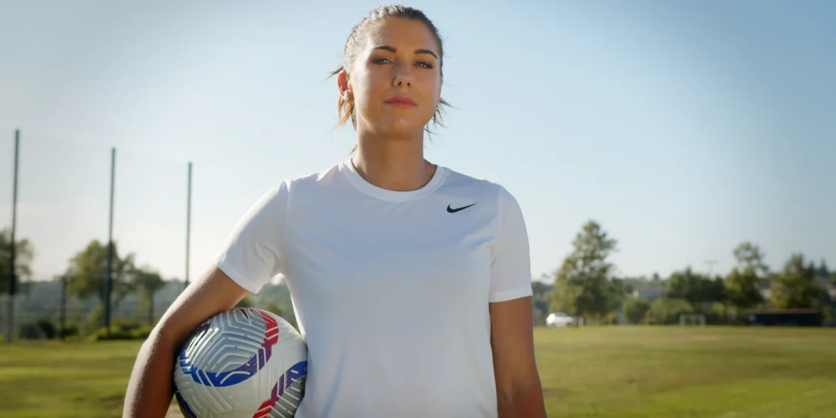 an image of former soccer star Alex Morgan holding a soccer ball on a field