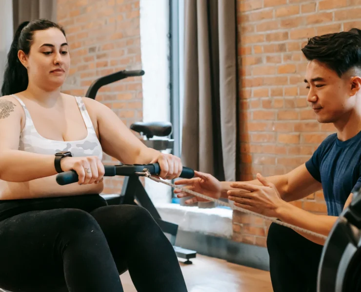 obese woman on rower, personal trainer beside her