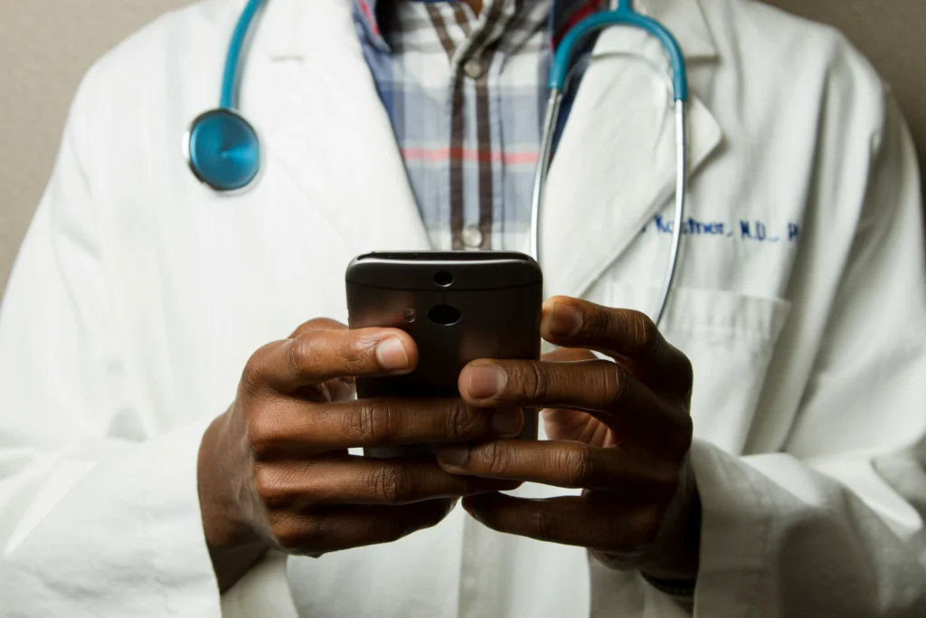 An image of a male doctor in a white lab coat who is looking at a cellular phone.