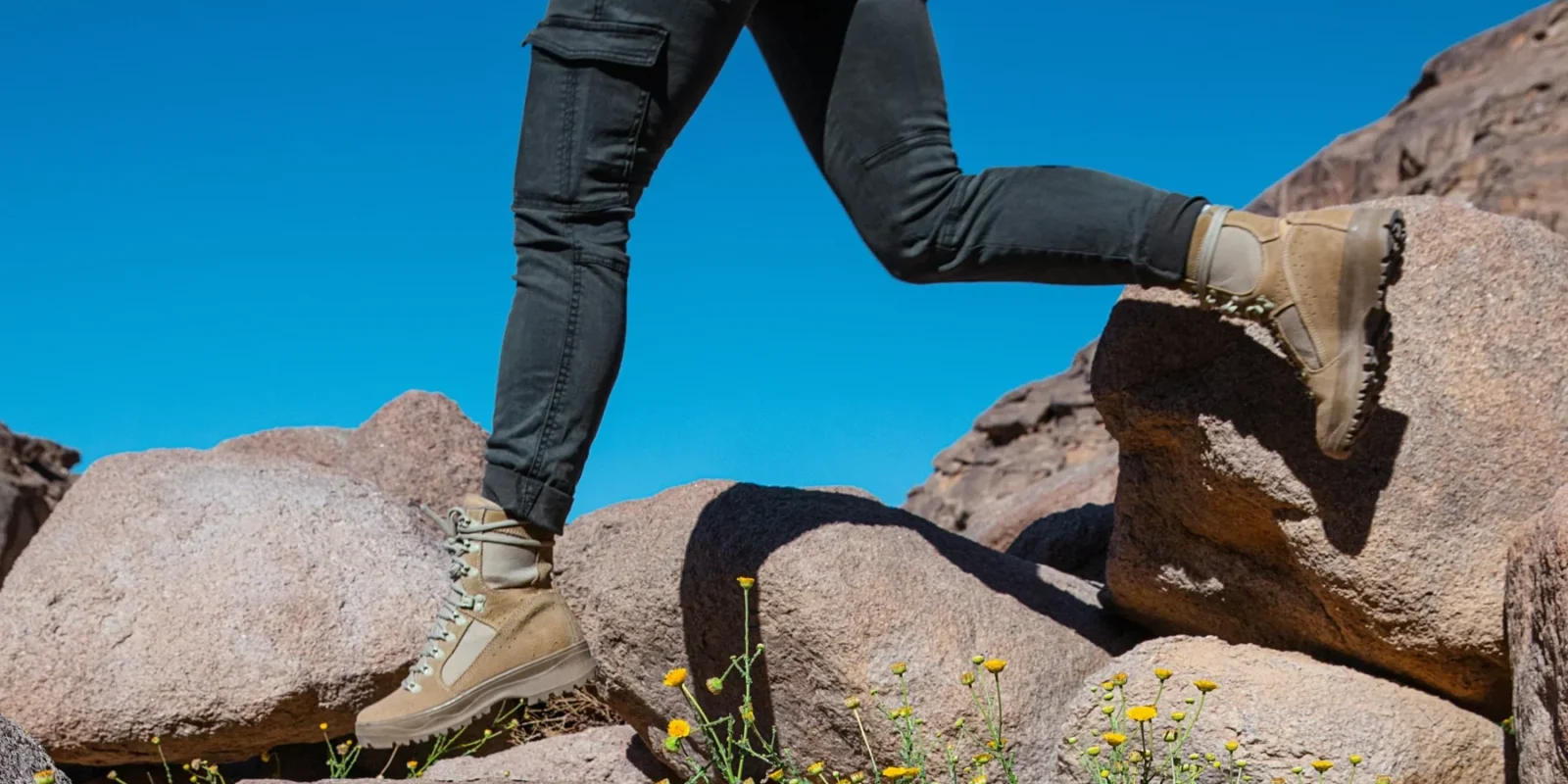 A cropped image showing the bottom half of a body walking along a rocky landscape with flowers.