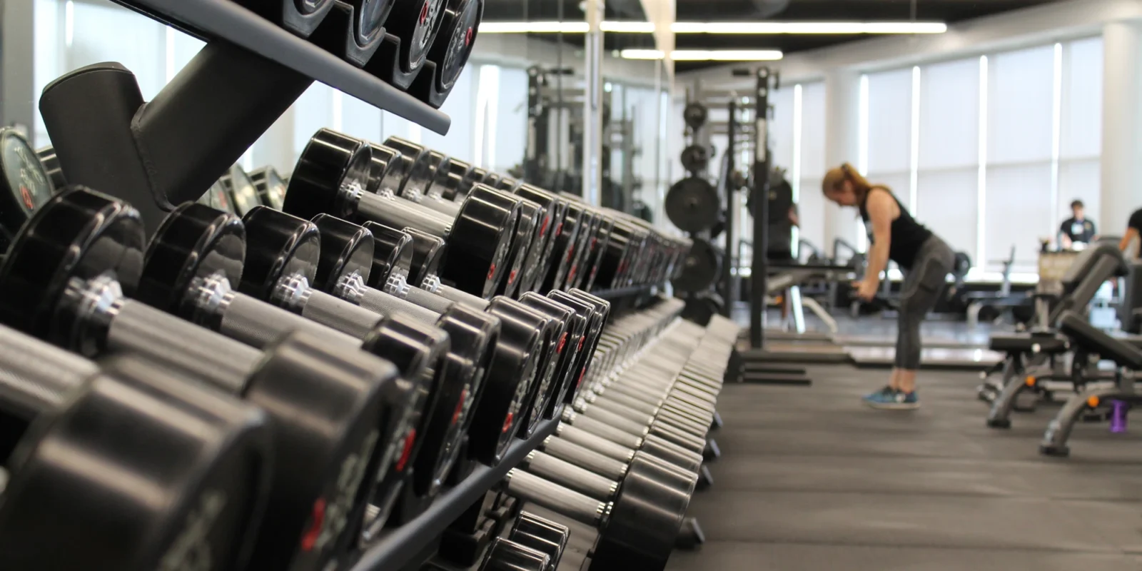 an image of a weight rack at a gym with a woman standing at the end lifting weights