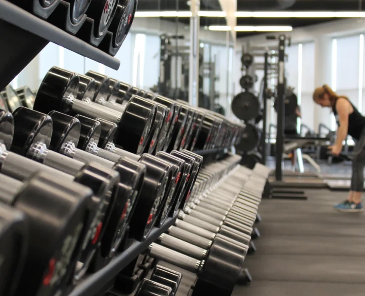 an image of a weight rack at a gym with a woman standing at the end lifting weights