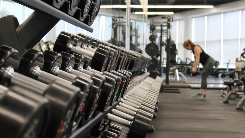 an image of a weight rack at a gym with a woman standing at the end lifting weights