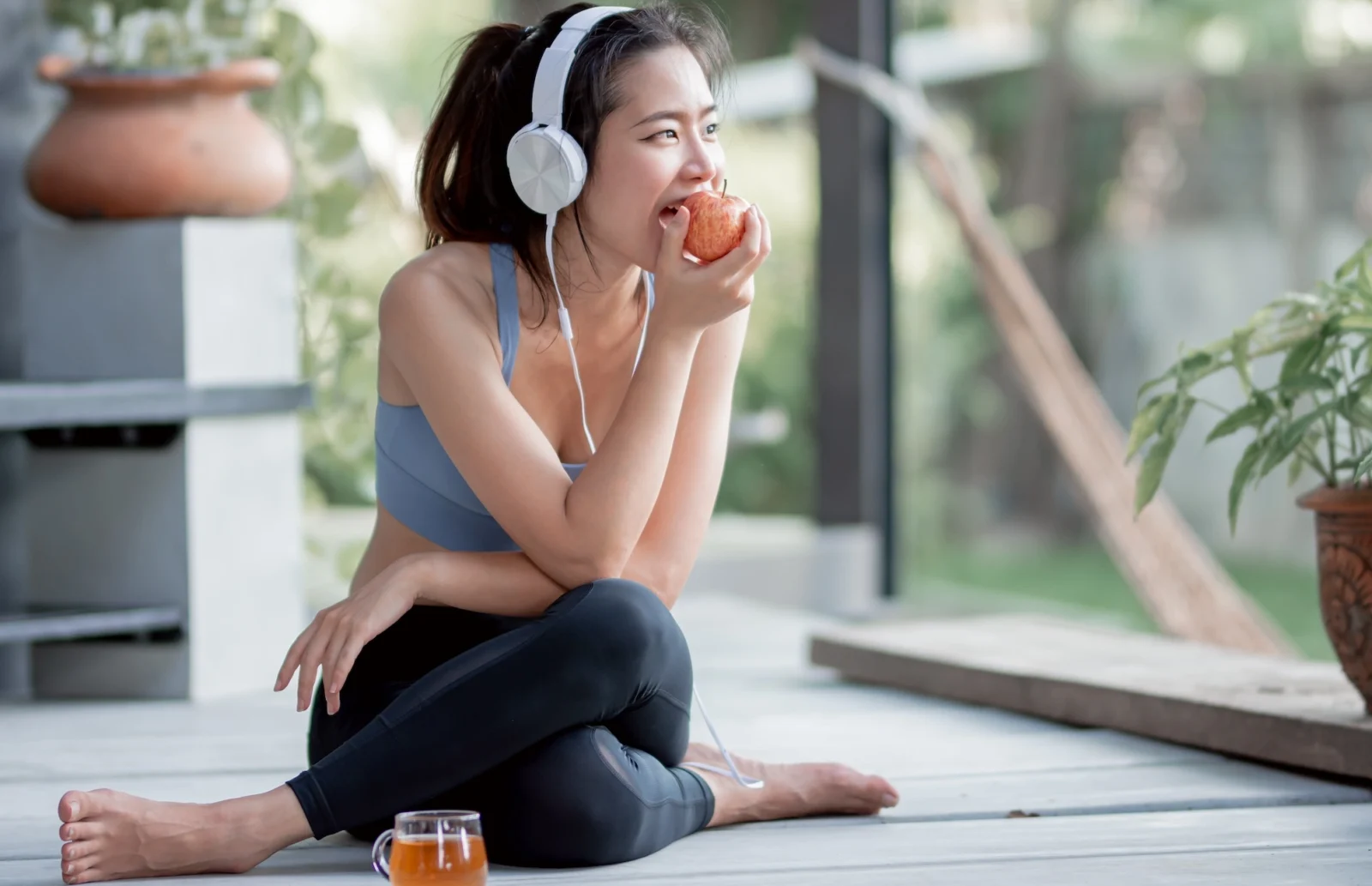 fitness-focused woman eats an apple while listening to music on headphones