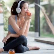 fitness-focused woman eats an apple while listening to music on headphones