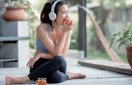 fitness-focused woman eats an apple while listening to music on headphones