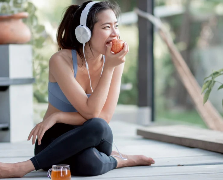 fitness-focused woman eats an apple while listening to music on headphones