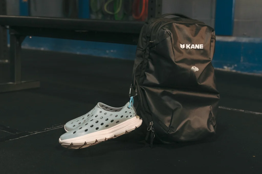 A pair of green Kane shoes next to a backpack