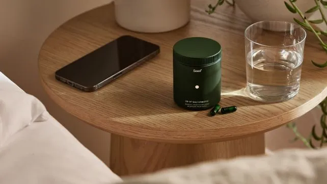 Seed probiotic on a table next to a phone and glass of water