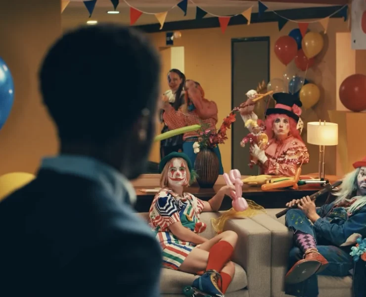 man looks surprised at a living room full of clowns