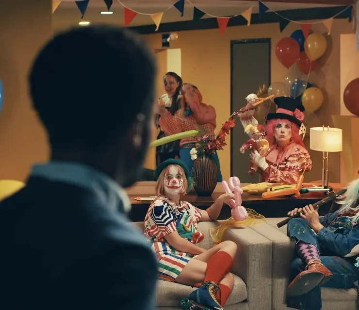 man looks surprised at a living room full of clowns