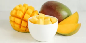 a cup of diced mango next to a whole mango