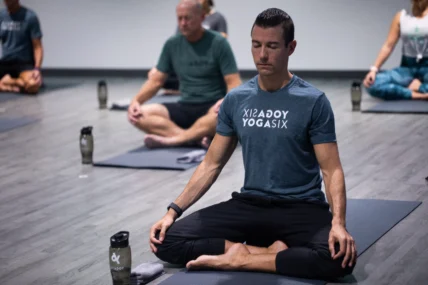 a man meditating on a yoga mat wearing a YogaSix t-shirt.