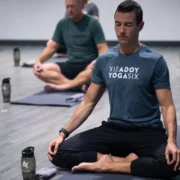 a man meditating on a yoga mat wearing a YogaSix t-shirt.