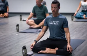 a man meditating on a yoga mat wearing a YogaSix t-shirt.