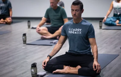 a man meditating on a yoga mat wearing a YogaSix t-shirt.