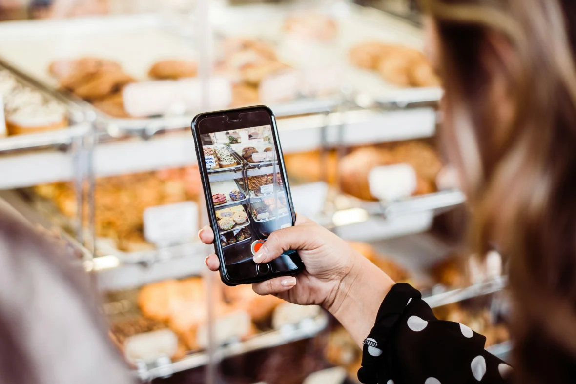 A woman using her phone camera to take a picture of baked goods.
