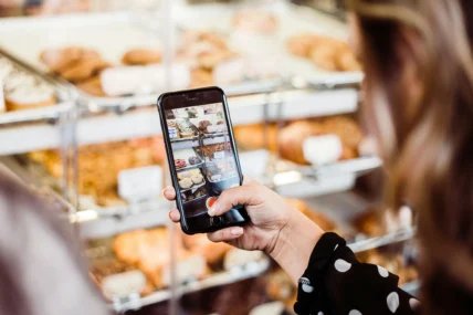 A woman using her phone camera to take a picture of baked goods.