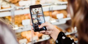 A woman using her phone camera to take a picture of baked goods.