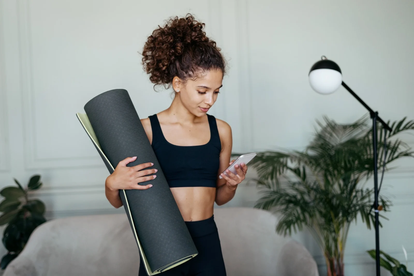 woman with a yoga mat looks at her phone