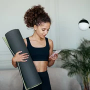 woman with a yoga mat looks at her phone