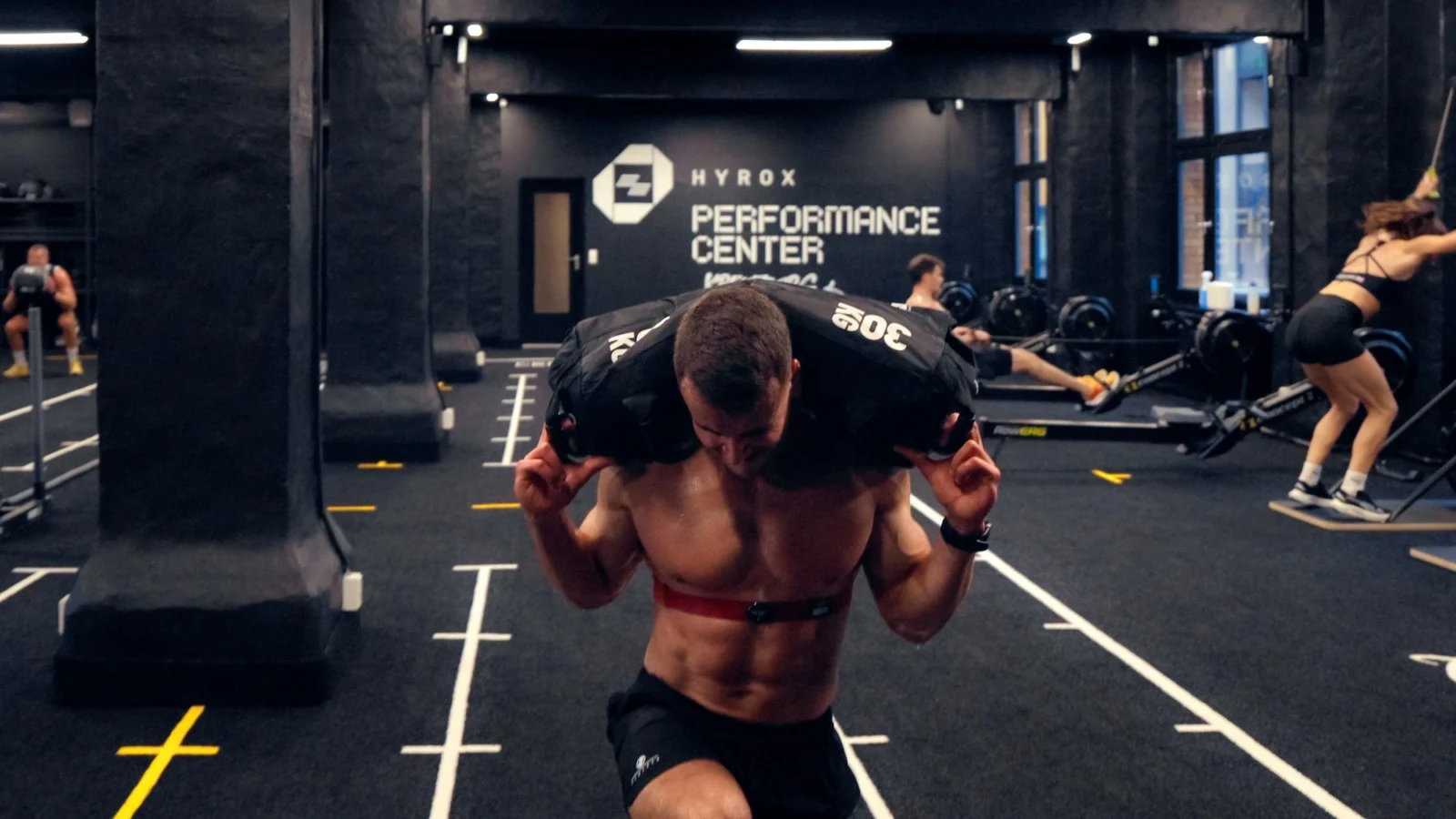 man carries a sandbag inside a Hyrox training club