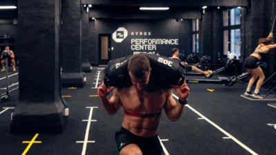 man carries a sandbag inside a Hyrox training club