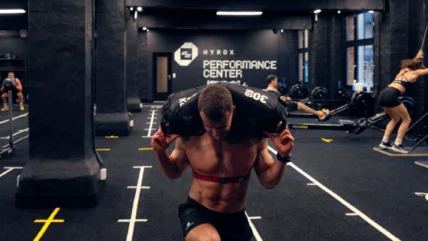 man carries a sandbag inside a Hyrox training club