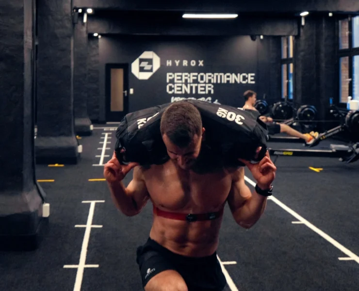 man carries a sandbag inside a Hyrox training club