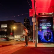 A man standing outside at night near a Thatch billboard.