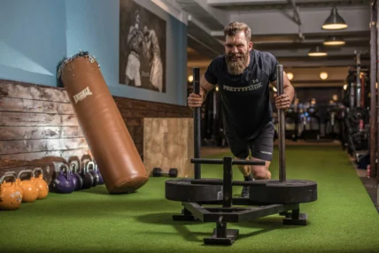 A man pushing a sled on indoor turf.
