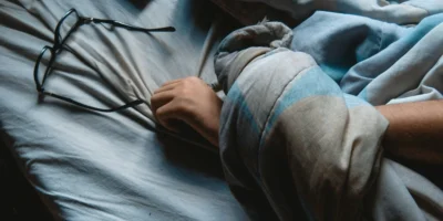 A person sleeping in bed with glasses nearby.