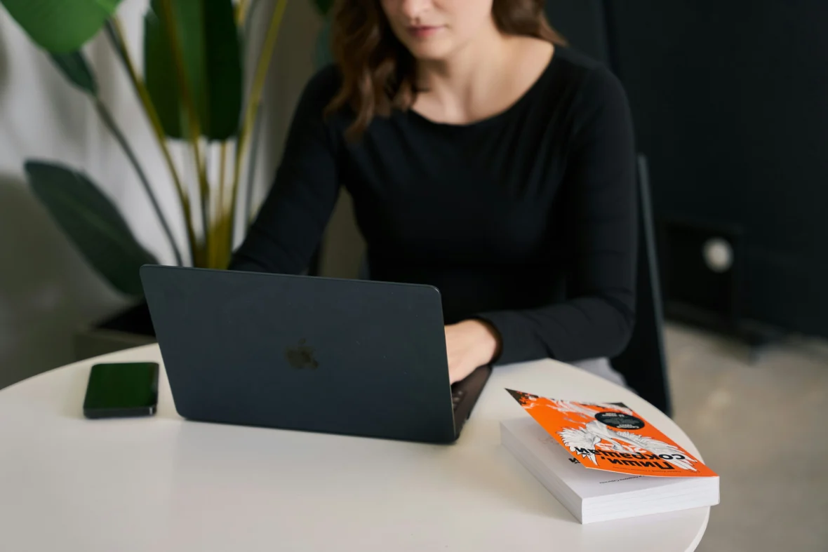 a woman on her laptop with a book nearby.