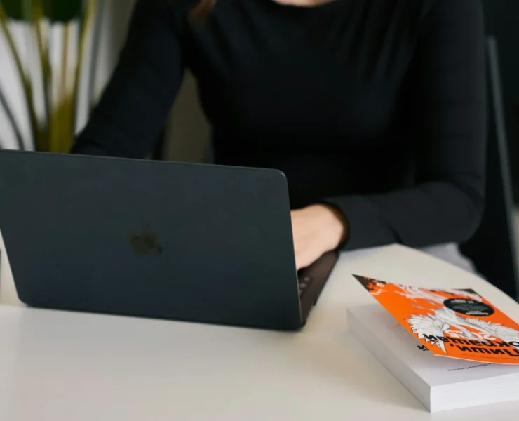 a woman on her laptop with a book nearby.