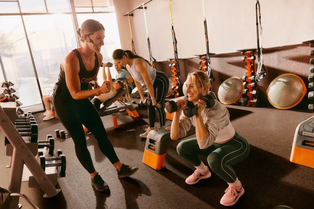 woman squats with dumbbells inside an Orangetheory Fitness studio