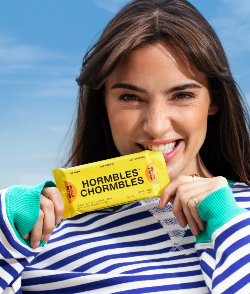 woman bites the wrapper of a Hormbles Chormbles protein bar